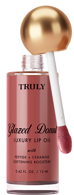A pink bottle of Truly Lip Oil Glazed Donut with a gold cap is displayed next to a glazed donut, with a purple lip oil smear in the background.