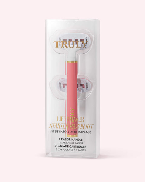 A pink razor kit in clear packaging, labeled Life Shaver Starter Razor from Truly Beauty. Made for sensitive skin, it includes a razor handle and two 5-blade cartridges. Set against a light pastel pink background.