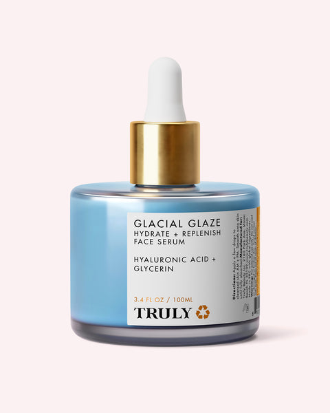 A blue bottle of Truly Beauty’s Glacial Glaze Hydrate + Replenish Face Serum with a gold dropper lid, labeled Hyaluronic Acid + Glycerin and 3.4 fl oz / 100ml, is shown against a pale background—formulated to boost skin elasticity and provide intense hydration.