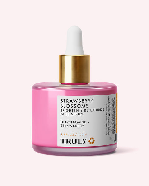A pink bottle of Truly Beauty's Strawberry Blossoms Brighten + Retexturize Face Serum, topped with a gold dropper cap and white label, featuring details about niacinamide and strawberry extract to help brighten skin.