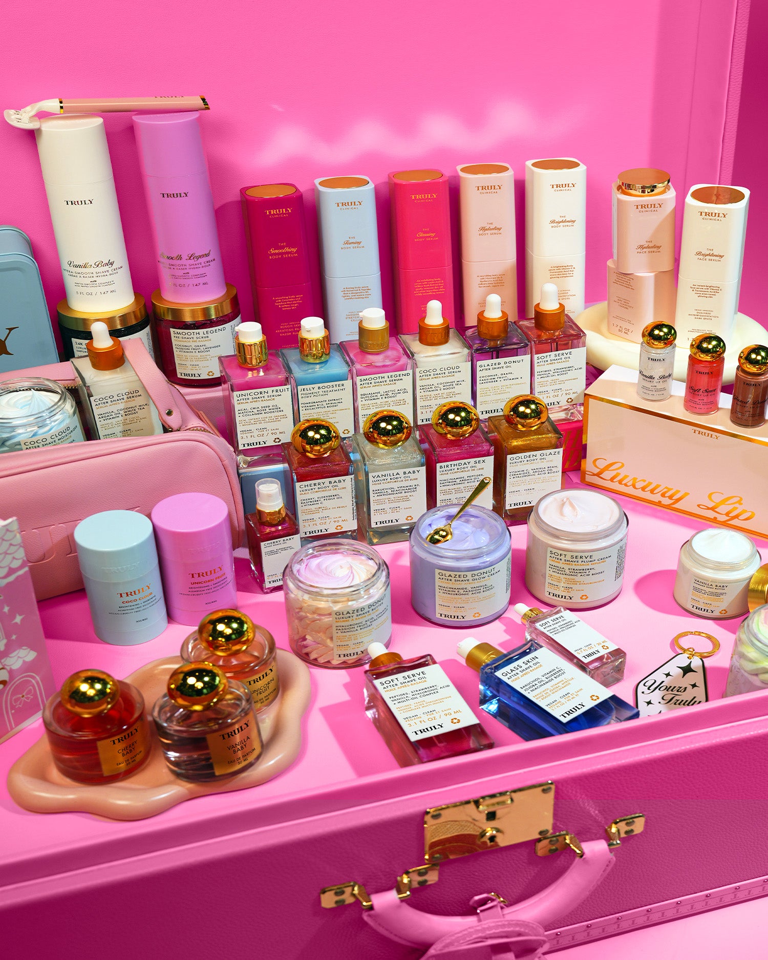 The Black Friday 2025 Mystery Bag #1 by Truly Beauty features a pink suitcase packed with beauty and skincare essentials—bottles, jars, and boxed goodies—arranged against a vibrant pink background, ideal for holiday shopping or as a festive surprise.