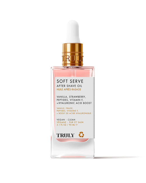 A glass dropper bottle of Soft Serve After Shave Oil features a gold cap, clear pink liquid, and a white label listing ingredients like vanilla, strawberry, peptides, vitamin F, and hydrating hyaluronic acid.
