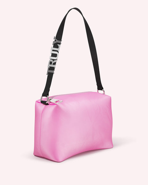 The Signature Crystal Pouch by Truly Beauty is a rectangular pink handbag (7.1x4.6x2.5 in) with a black shoulder strap and large silver TRULY letters, boasting a simple, modern design against a plain light background.