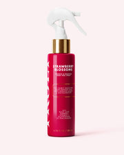 A red spray bottle labeled “Strawberry Blossom Smooth & Brighten Body Peel Spray” by Truly Beauty, featuring gold and white accents, sits on a light pink background. The label highlights benefits such as smoother skin, reducing dark spots, and targeting keratosis pilaris with kojic acid.