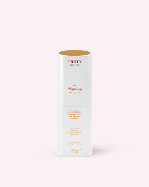 A white bottle of Truly Beauty The Brightening Face Serum with gold and brown text stands upright on a light pink background. This face serum helps improve skin brightness and reduce hyperpigmentation.