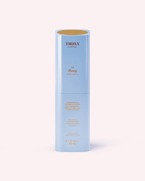 A cylindrical light blue bottle labeled Truly Beauty The Firming Body Serum stands upright on a light pink background, featuring orange and gold text.