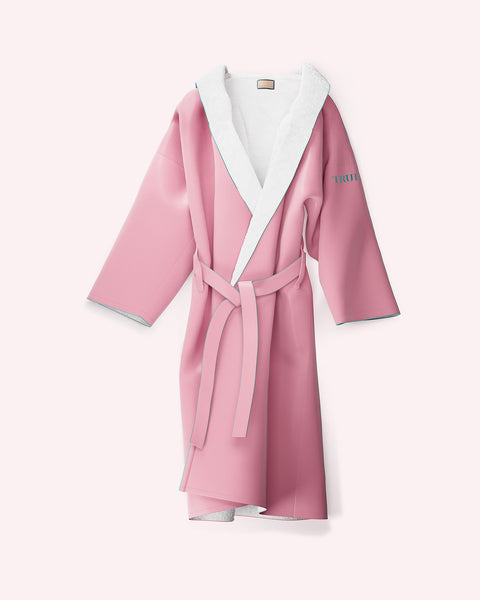 The Truly Beauty Signature Luxury Bathrobe is a pink, one-size-fits-all robe with a white collar and lining, soft polyester fabric, matching waist belt, and TRUTH in blue on the left sleeve. Displayed on a light pink background.