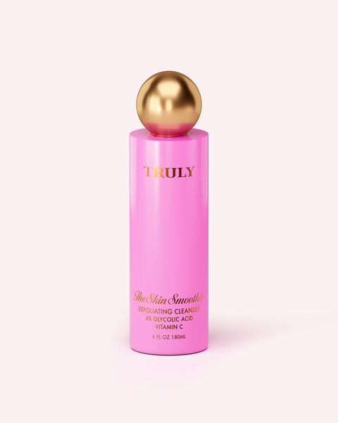 A tall, pink bottle of Truly Beauty Skin Smoothie Gentle Facial Cleanser with a shiny gold spherical cap is displayed on a light background.