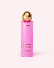 A pink bottle of Truly Beauty’s Skin Smoothie Gentle Facial Cleanser, featuring gold text and a gold spherical cap, sits on a light pink background. The hydrating formula with hyaluronic acid comes in a 5 fl oz (148 mL) size.