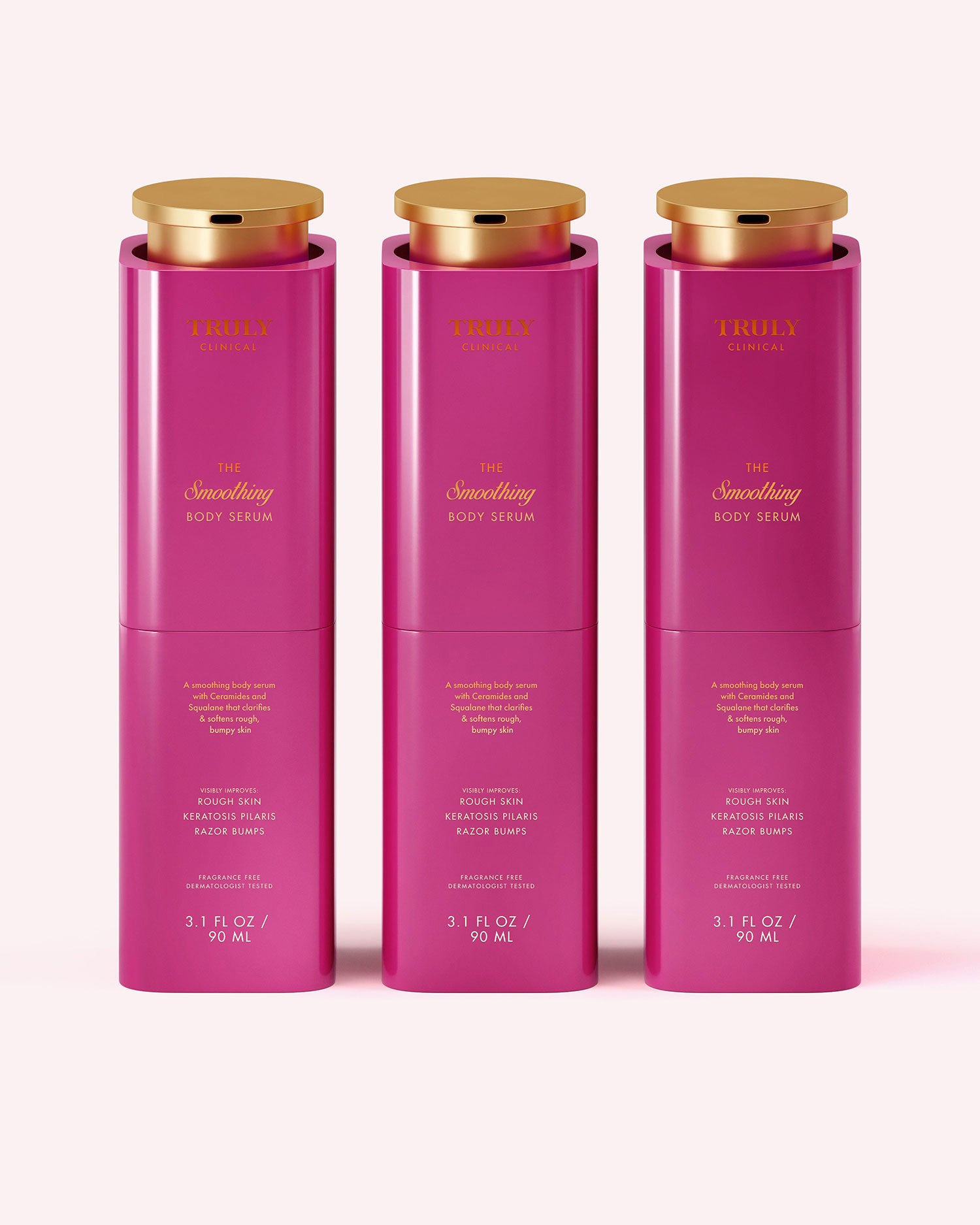 Three pink, cylindrical bottles of Truly Beauty The Smoothing Body Serum (3.1 fl oz/90 ml each) with gold caps are lined up side by side on a pale pink background. This serum targets rough, bumpy skin and keratosis pilaris.