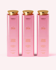 Three pink bottles of Truly Beauty The Hydrating Body Serum with gold caps are lined up on a pale pink background. Each 3.1 fl oz (90 ml) serum hydrates skin and is infused with niacinamide for a visibly smoother, firmer look.