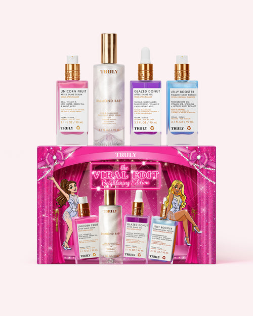 A set of four Truly Beauty skincare bottles displayed above their matching pink gift box. The set includes a pink bottle, a clear bottle with a gold cap, a purple bottle, and a blue bottle, all with gold caps, arranged on a light pink background.
