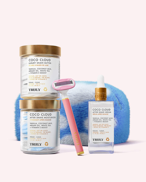 The Truly Beauty Ultimate Coco Cloud Shave Set, featuring shave cream, post-shave serum, a pink and gold razor, and a plush pouch, is displayed against a light pink background.
