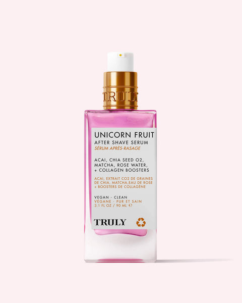 A pink and white 3.1 fl oz bottle of Truly Beauty Unicorn Fruit After Shave Serum with a gold pump, featuring vegan, clean ingredients like acai and chia seed oil to soothe post-shave redness and prevent ingrowns.