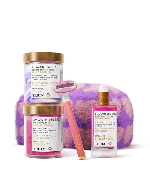 The Truly Beauty Ultimate Smooth Legend Shave Set includes Glazed Donut and Smooth Legend skincare, two jars, a bottle, a razor, and a purple-and-pink fuzzy case—all arranged on a light pink background.