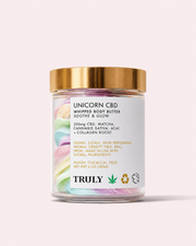 A glass jar topped with a gold lid holds pastel rainbow whipped body butter. The label displays Unicorn CBD Soothe & Glow Whipped Body Butter, featuring soothing ingredients like CBD and matcha to help calm inflammation. The brand name Truly Beauty appears at the bottom, with the playful phrase “Unicorn Hemp” included on the packaging.