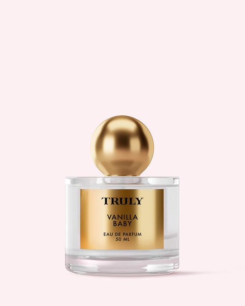 Truly Beauty’s Vanilla Baby Eau De Parfum, 50 ml, features a gold label and large gold cap, shown on a pale pink background—infused with warm amber notes for a gentle sweetness.