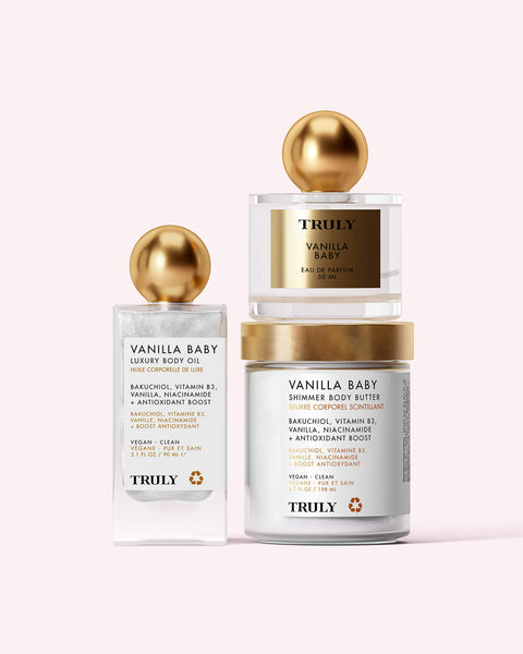 The Vanilla Baby Luxury Trio by Truly Beauty features body oil, shimmer body butter, and perfume—each with gold lids and white labels on a light pink background. Enjoy their warm vanilla scent for glowing, radiant skin all day.