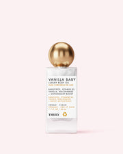 A bottle of Truly Beauty Vanilla Baby Luxury Body Oil with a gold spherical cap and white label, featuring black and gold text, sits against a pale pink background. The label touts plumping, anti-aging benefits, key ingredients, and product features.