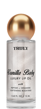 A clear bottle of Truly Lip Oil Vanilla Baby with a gold cap sits on a white background, accented by a white flower and a swirl of creamy product behind it.
