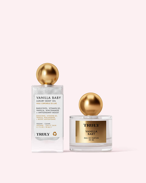 The Vanilla Baby Fragrance Duo by Truly Beauty—luxury body oil and eau de parfum, both with gold spherical caps—is beautifully displayed on a pale pink background.