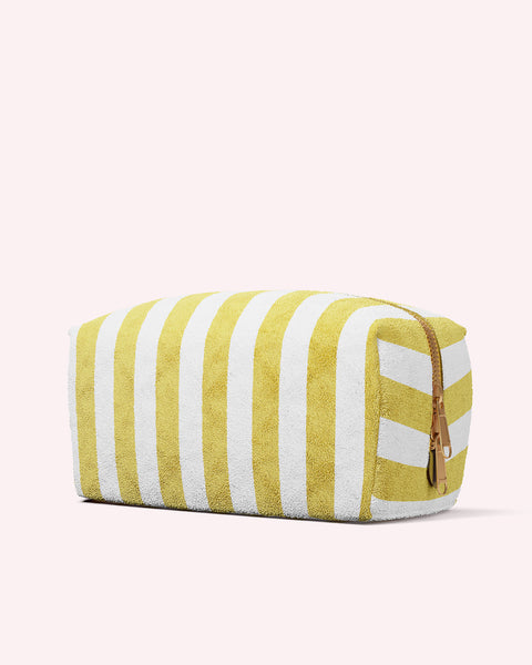 The Truly Beauty Luxury Terry Case features yellow and white vertical stripes, a textured finish, and a brown zipper, shown against a light pink background.