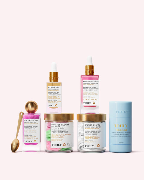 Truly Beautys Zaras Ultimate Routine—featuring oils, body butter, and a deodorant stick—is arranged with a gold spoon on a pale pink background, perfect for achieving that cool girl glow.