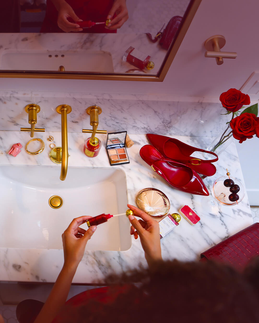 	
Two people at a marble sink apply Truly Lip Oils by Truly, surrounded by makeup, jewellery, a handbag, red high heels, perfume, a chocolate bar, roses, and sparkling wine for an elegant and festive vibe.