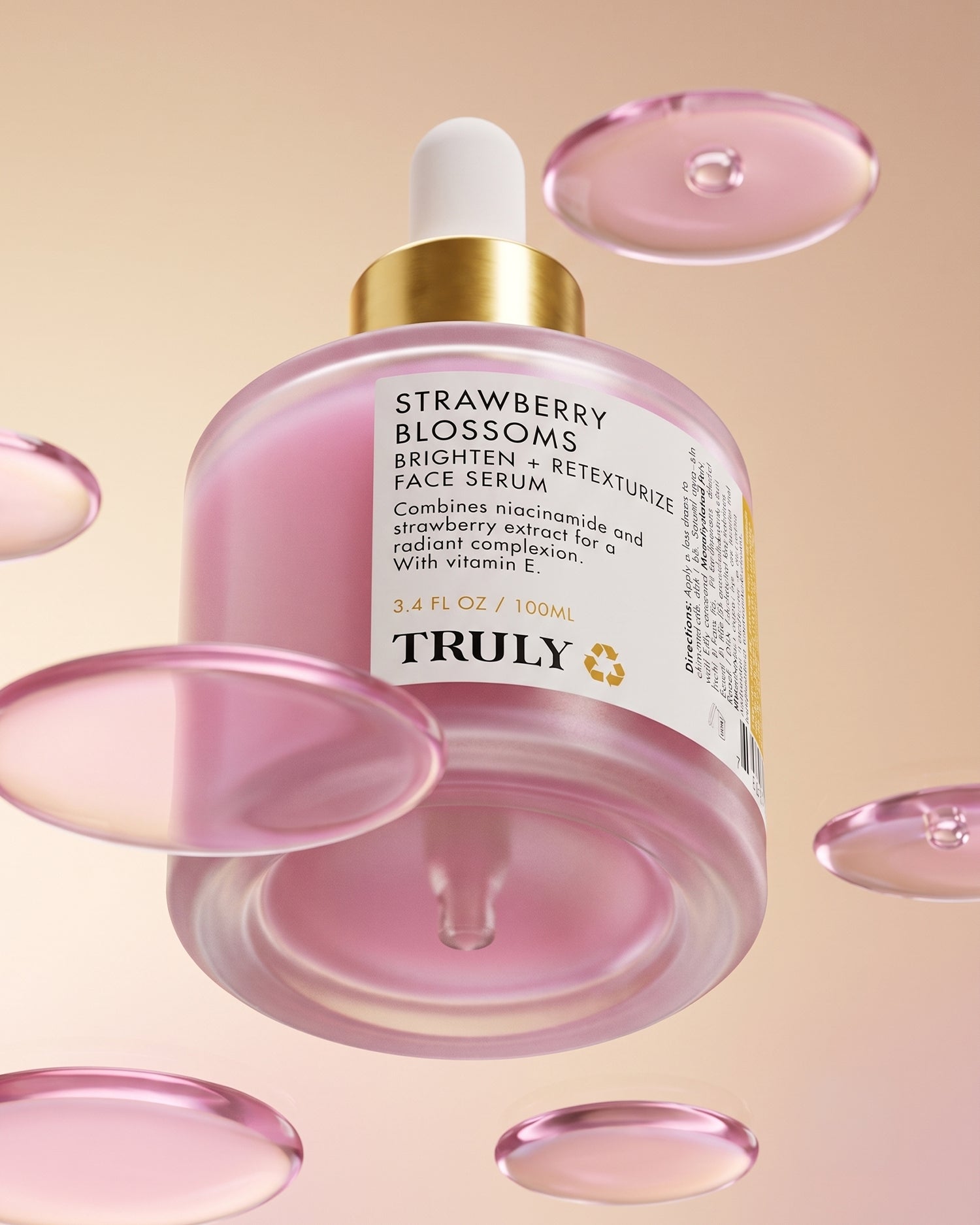 A pink bottle of Truly Beauty’s Strawberry Blossoms Brighten + Retexturize Face Serum, complete with a dropper, is showcased amid pink liquid droplets on a soft pink background. Formulated with strawberry extract, niacinamide, and nourishing vitamin E, the label emphasizes its skin-brightening benefits.