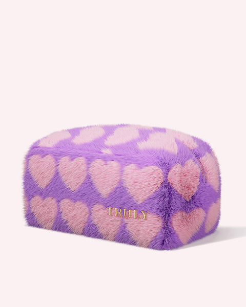 The Amanda Cerny Shave Kit Bag by Truly Beauty is a rectangular, furry, purple pouch with pink heart patterns and TRULY embroidered in gold—perfect for your skincare routine, shown against a plain light background.